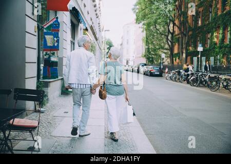 Full length of retired couple holding hands while walking on sidewalk in city Stock Photo