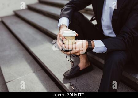 Low section of businessman with disposable cup and smart phone sitting on staircase Stock Photo