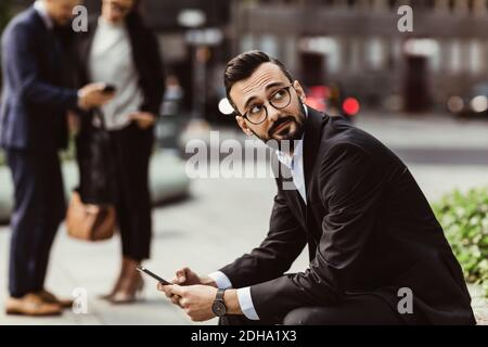 Businessman looking up while using mobile phone outdoors Stock Photo