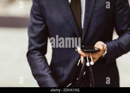 Midsection of male entrepreneur using smart phone while standing outdoors Stock Photo