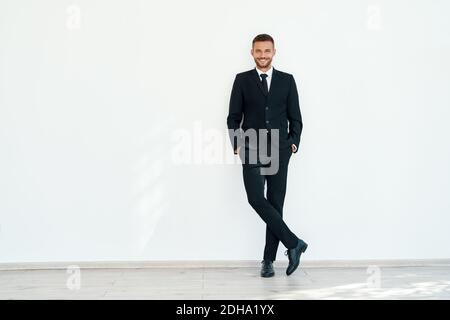 Smiling confident businessman in elegant suite posing on white wall background Stock Photo