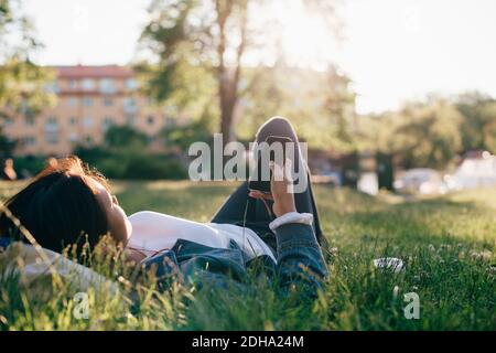 Teenage girl using smart phone while lying on grass Stock Photo