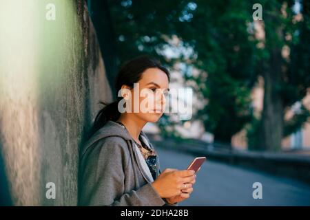 Side view of young woman holding smart phone while looking away Stock Photo