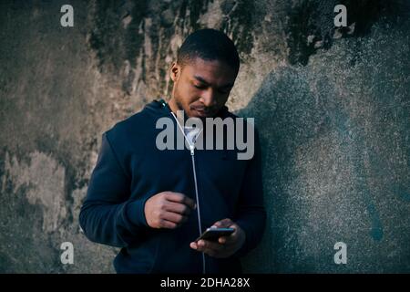 Young man leaning on wall while using smart phone Stock Photo