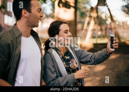 Cheerful woman showing smart phone to male friend Stock Photo