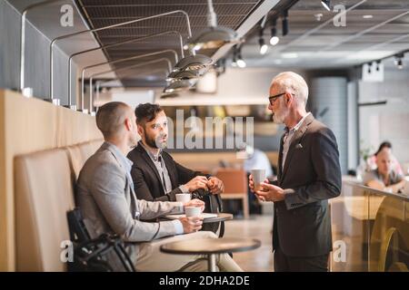 Senior businessman talking with male coworkers during coffee break in office Stock Photo