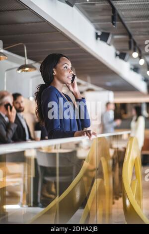 Female executive talking on mobile phone while standing by railing in office Stock Photo
