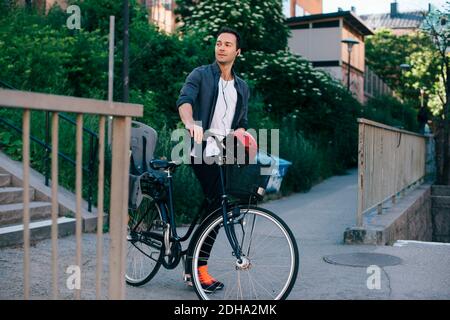 Mid adult man walking with bicycle on footpath in city Stock Photo