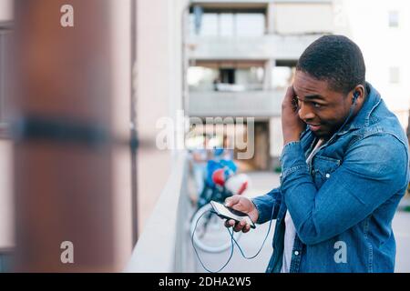 Young man adjusting headphones while standing on footbridge in city Stock Photo