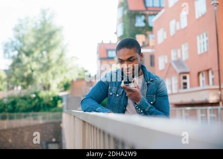 Young man talking on smart phone while standing by railing Stock Photo