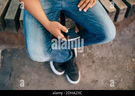 Low section of young man using smart phone while sitting on bench in city Stock Photo
