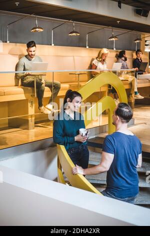 Male and female professionals talking on staircase while colleagues working in office Stock Photo