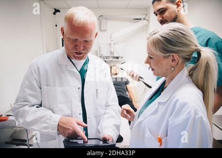 Doctors discussing over digital tablet while patient lying on bed at hospital Stock Photo