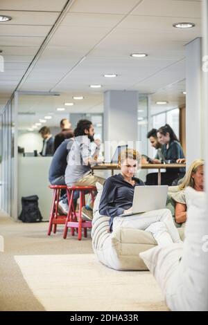 Businesswoman using laptop while colleagues working in background at office Stock Photo