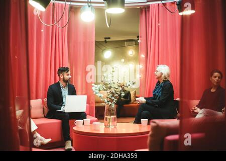 Young businessman using laptop while discussing business strategies with coworker in office Stock Photo