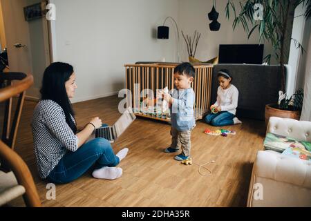 Mother using laptop while working from home sitting with children in living room Stock Photo