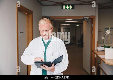 Mature doctor using digital tablet while standing in hospital corridor Stock Photo
