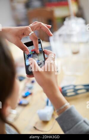 Cropped image of young female technician touching mobile screen while photographing model on table at workshop Stock Photo
