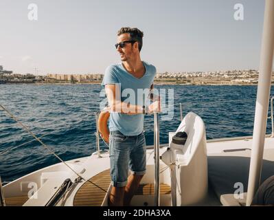 Mature man wearing sunglasses sailing boat in sea against sky Stock Photo