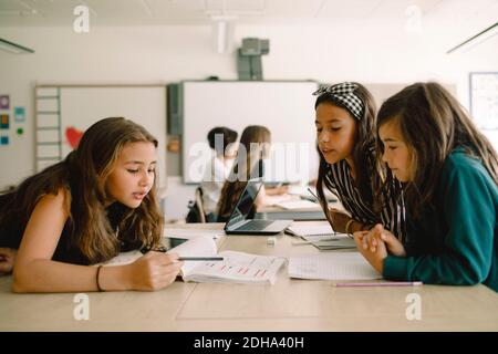 Female students studying from book while sitting by table in classroom Stock Photo