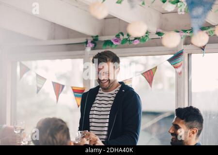Smiling young man standing with friends holding wineglasses at home Stock Photo
