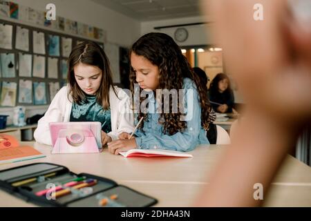 Female students using tablet at table in classroom Stock Photo