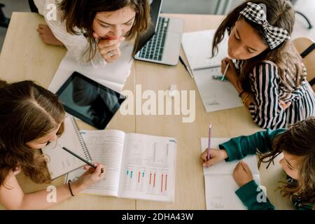 High angle view of students with female tutor studying from book at table in classroom Stock Photo