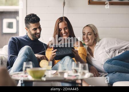 Cheerful young friends sharing digital tablet while sitting on sofa at home Stock Photo