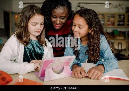 Female tutor with students looking at digital tablet in classroom Stock Photo