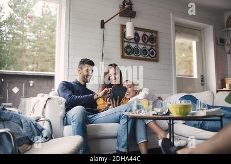 Young man sharing digital tablet with female friends on sofa at home Stock Photo