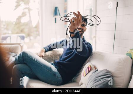 Cheerful man holding electrical cable while sitting on sofa at home Stock Photo