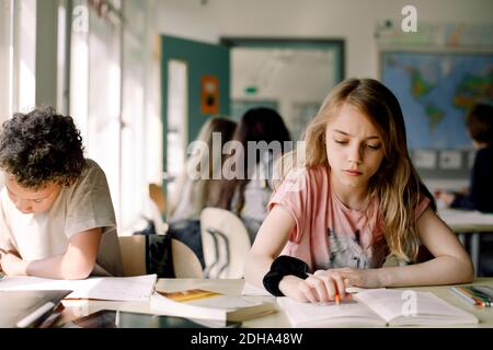 Female student studying from book while sitting by male friend in classroom Stock Photo