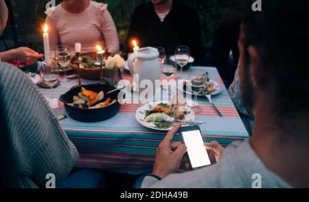 Cropped image of young man using smart phone while having dinner with friends Stock Photo