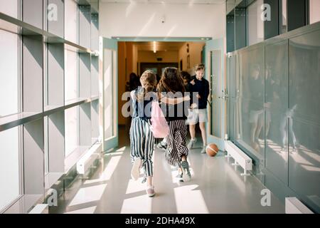 Rear view of female friends running in school corridor Stock Photo