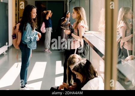 Female students communicating in school corridor during lunch break Stock Photo