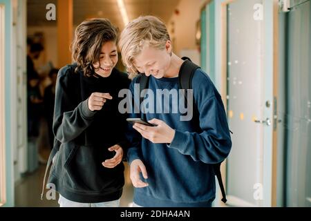 Smiling male students using smart phone in school corridor Stock Photo