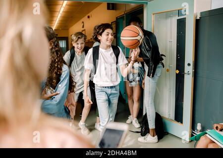 Playful male students walking with basketball in school corridor during lunch break Stock Photo