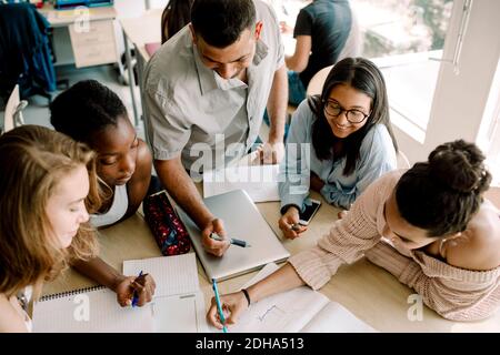 High angle view of teenagers studying while professor standing by table in classroom Stock Photo