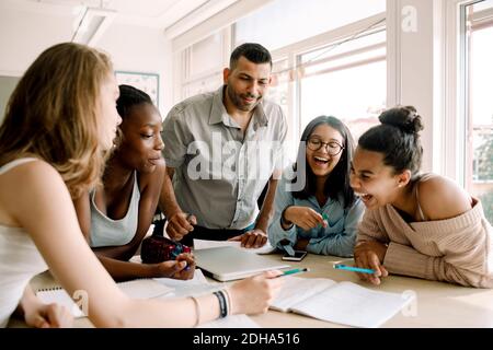 Cheerful female teenagers studying while professor standing by table in classroom Stock Photo
