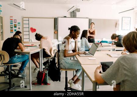 Junior high students studying while female teacher standing in classroom Stock Photo