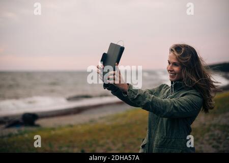 Smiling young woman taking selfie on digital tablet at beach Stock Photo