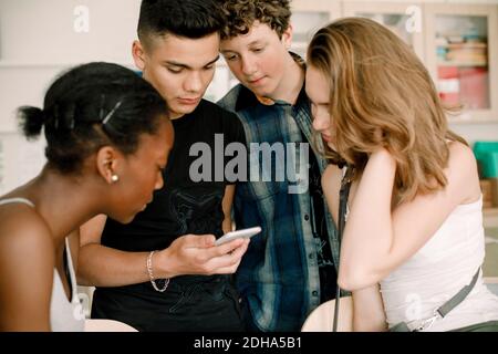 Male student using phone while standing by friends in classroom Stock Photo