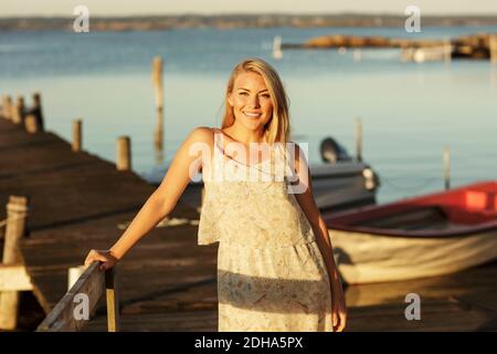 Portrait of smiling blond woman standing by railing at jetty Stock Photo