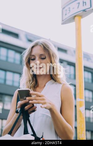 Smiling female entrepreneur using smart phone against building in city Stock Photo
