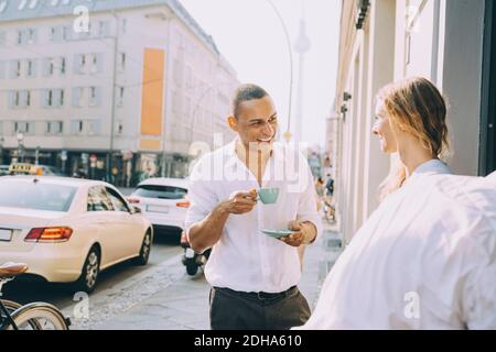 Smiling businessman drinking coffee with female coworker on sidewalk cafe in city Stock Photo
