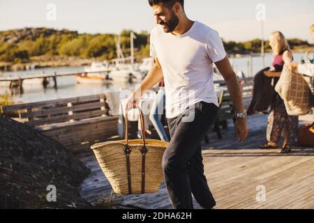 Man carrying picnic basket while walking on jetty during sunny day Stock Photo