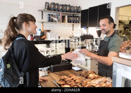 Smiling mature male owner serving food package to female customer at checkout in bakery Stock Photo