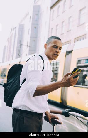 Male entrepreneur with bicycle using smart phone in city Stock Photo