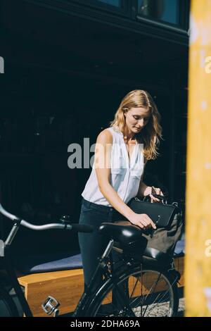 Young businesswoman holding bag on bicycle on street in city Stock Photo