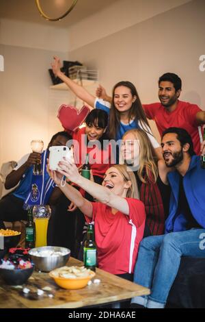 Cheerful friends taking selfie with instant camera while watching sports at home Stock Photo